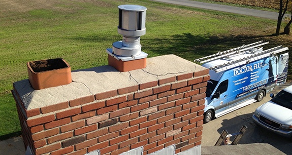 Eine rissige, reparaturbedürftige Schornsteinkrone mit einem Doctor Flue-Truck im Hintergrund.